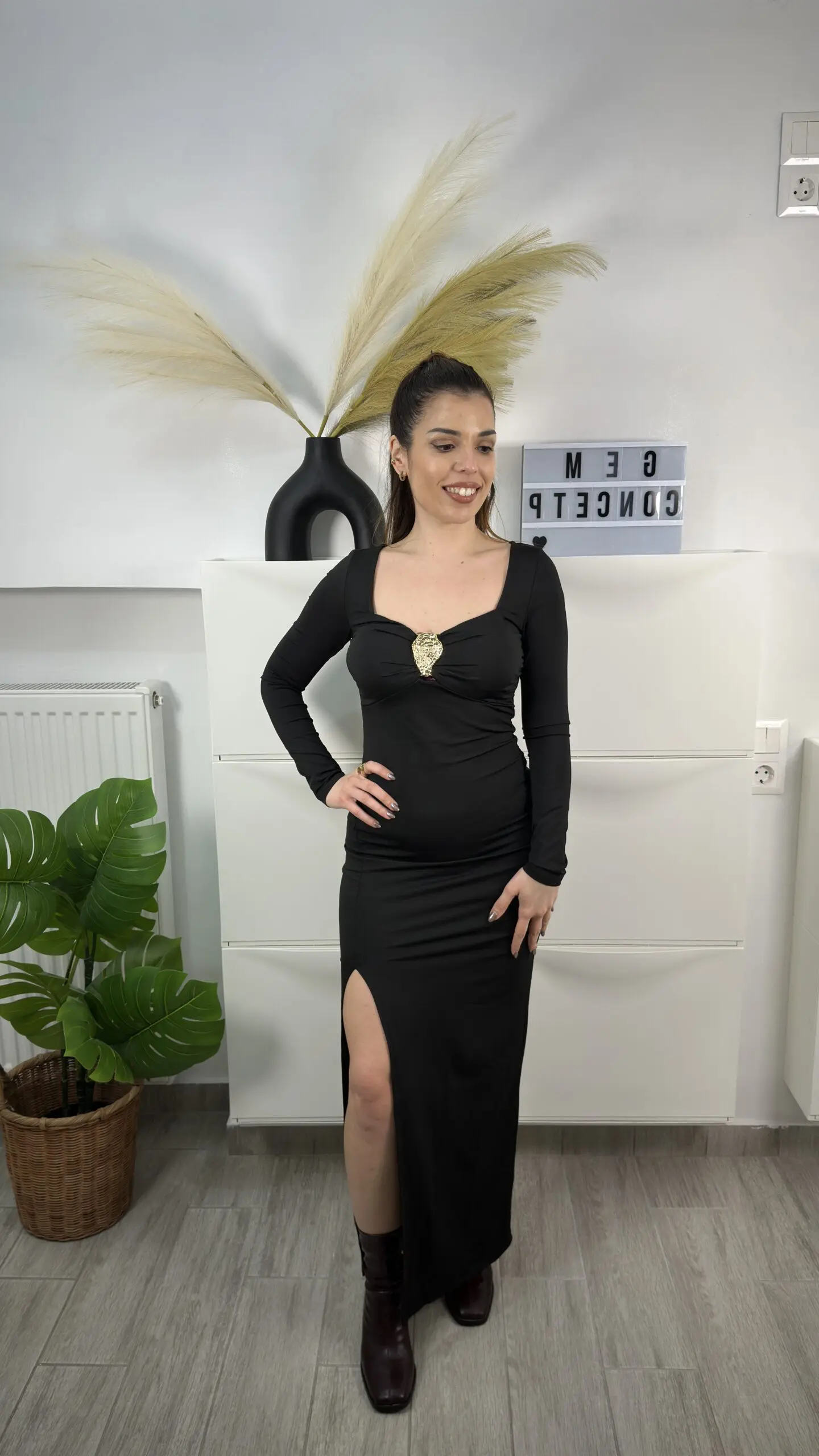 Μοντέλο που φοράει μαύρο μακρύ φόρεμα με σκίσιμο στο πόδι και ποζάρει σε λευκό φόντο